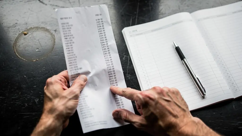 Des mains comparent un relevé bancaire à un registre comptable sur un bureau.